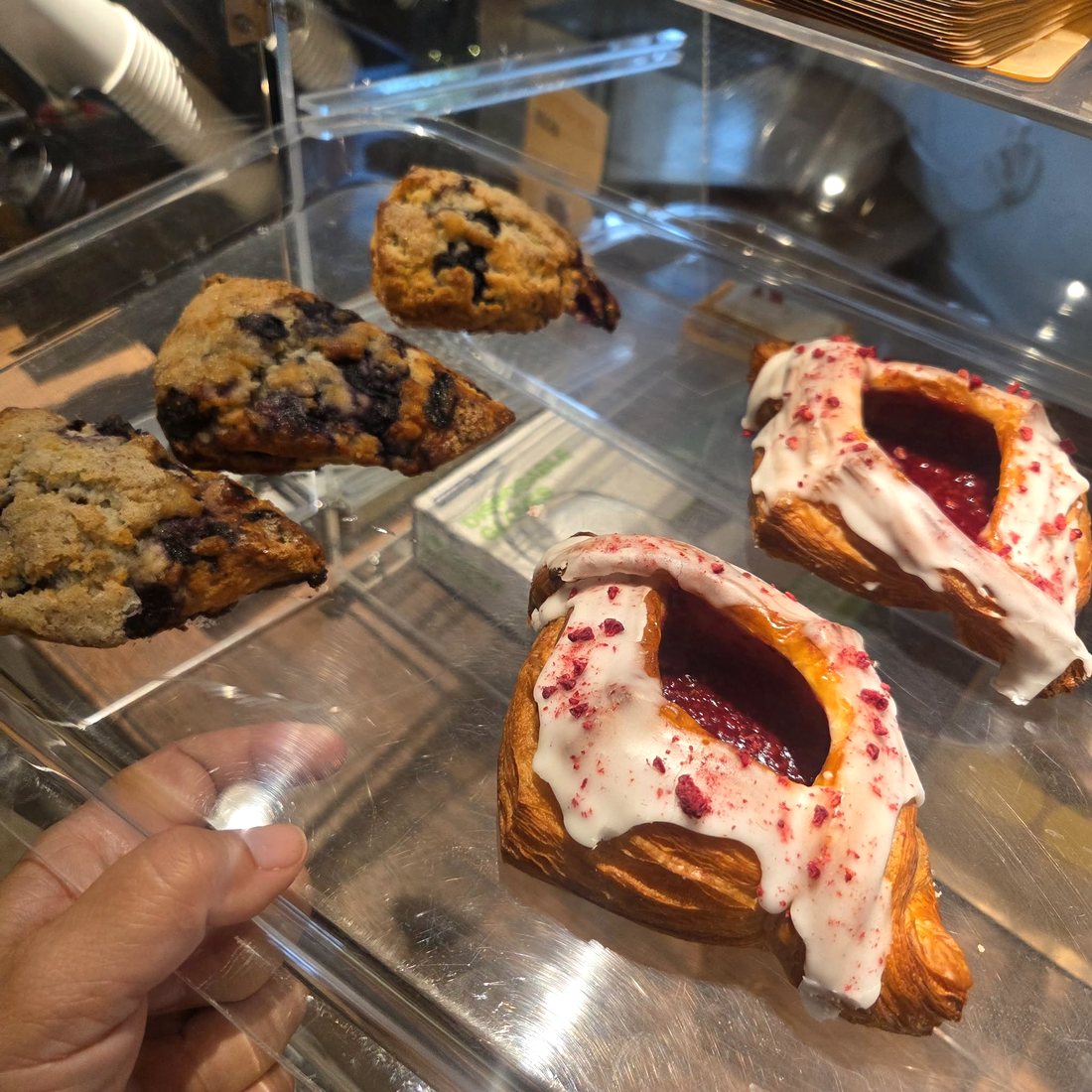 The pastry case at Icebergs holding blueberry scones and two raspberry danishes with white icing.